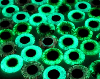 May include: A close-up of a group of green glow-in-the-dark plastic eyes. The eyes are round and have black pupils. They are arranged in a random pattern.