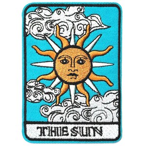 May include: A blue embroidered patch with a yellow sun with a face and white rays. The sun is surrounded by white clouds. The text "THE SUN" is at the bottom of the patch.
