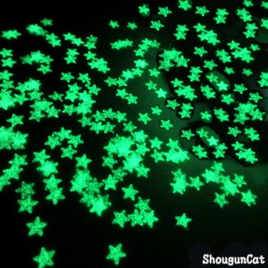 Pode incluir: Uma imagem de close-up de uma superfície escura coberta de adesivos em forma de estrela verde fluorescente. As estrelas estão espalhadas aleatoriamente pela superfície, criando um efeito de noite estrelada.