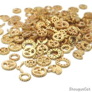 Könnte beinhalten: Ein großer Haufen goldfarbener Metallräder in verschiedenen Größen und Formen. Die Zahnräder sind auf einer weißen Oberfläche verstreut.