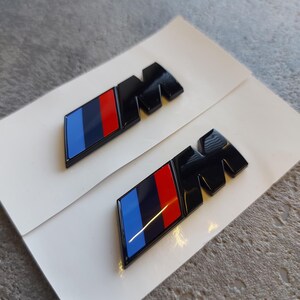 2x M side badges, 45 x 15 mm. Glossy black emblem - fender new badge