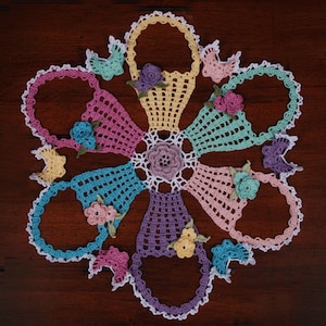 May include: A crocheted doily with a floral design in pastel colors. The doily is made up of eight sections, each with a different floral motif. The center of the doily features a large flower with a white center.