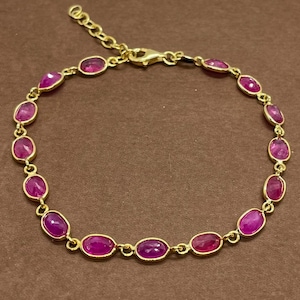 Può includere: Un bracciale a catena color oro caratterizzato da una serie di pietre preziose ovali di un vivace rosa magenta, distanziate uniformemente e incastonate in castoni metallici individuali, con una chiusura a moschettone sicura.