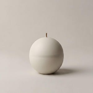 May include: A spherical, off-white candle with a single, thin wick. The candle has a smooth surface and a subtle horizontal line around its middle. The background is a neutral, light beige.