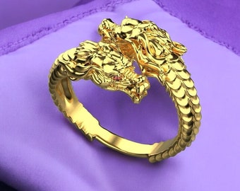 May include: A gold ring featuring two intertwined dragon heads with red gemstone eyes. The ring is made of a detailed, textured metal.