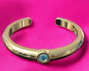 May include: A gold toe ring with a single blue gemstone.