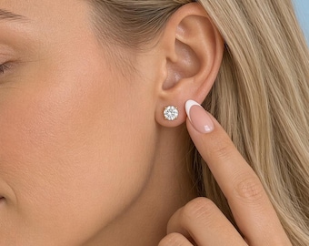 May include: A round, brilliant-cut clear gemstone stud earring set in a polished silver-toned metal prong setting. The earring is worn on the earlobe, featuring a single faceted stone that reflects light, creating a bright, sparkling appearance.