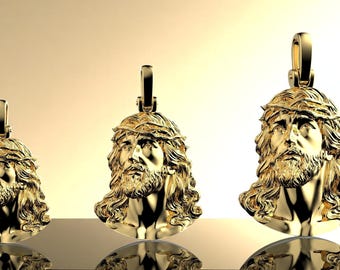 May include: Three gold-colored pendants in the shape of Jesus's head, each with a crown of thorns and a loop for a chain. The pendants are displayed on a reflective surface against a gradient background.