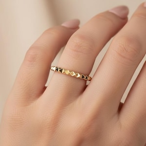 May include: A gold ring featuring a repeating pyramid pattern. The ring is displayed on a finger, highlighting its geometric design and polished appearance. The ring's design consists of small, raised pyramids around the band.