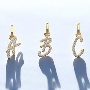 May include: Three gold pendants featuring a cursive letter design, each letter is encrusted with small clear diamonds.
