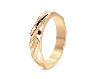 May include: A gold-colored ring with a unique, textured design. The ring's surface has an organic, flowing pattern, creating a wave-like appearance. The ring is set against a white background, highlighting its polished finish.
