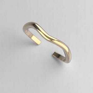 Puede incluir: Un brazalete abierto de color dorado con forma de onda. El brazalete está hecho de metal liso y tiene un diseño simple y moderno.