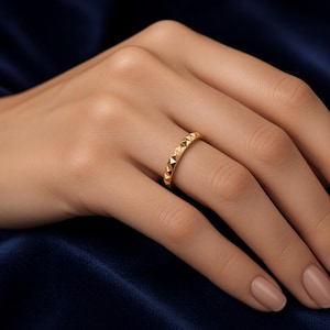 Könnte beinhalten: Ein goldener Ring mit einem sich wiederholenden Muster aus kleinen, erhabenen pyramidenförmigen Noppen rund um das gesamte Band. Das Metall hat eine polierte, reflektierende Oberfläche, die das Licht einfängt und eine Textur erzeugt.