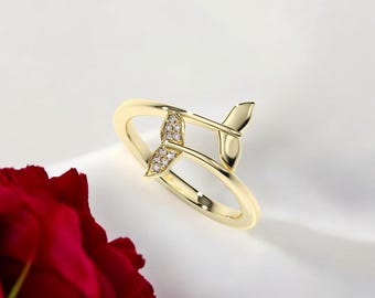 May include: A gold ring with a diamond-encrusted whale tail design. The tail is wrapped around the band of the ring.