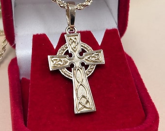 Puede incluir: Un collar de oro con un colgante de cruz celta y una cadena de cuerda. La cruz está detallada con intrincados nudos y se muestra en una caja de terciopelo rojo.