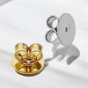 May include: Two earring backs, one gold-toned and one silver-toned, are displayed against a white background. The gold back is on the left, and the silver back is on the right. Both have a butterfly-style design for secure earring wear.