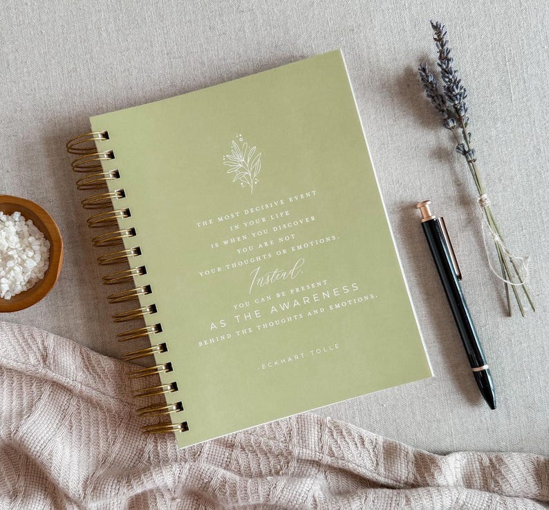 May include: A green spiral bound journal with a quote by Eckhart Tolle: "The most decisive event in your life is when you discover you are not your thoughts or emotions. Instead, you can be present as the awareness behind the thoughts and emotions."