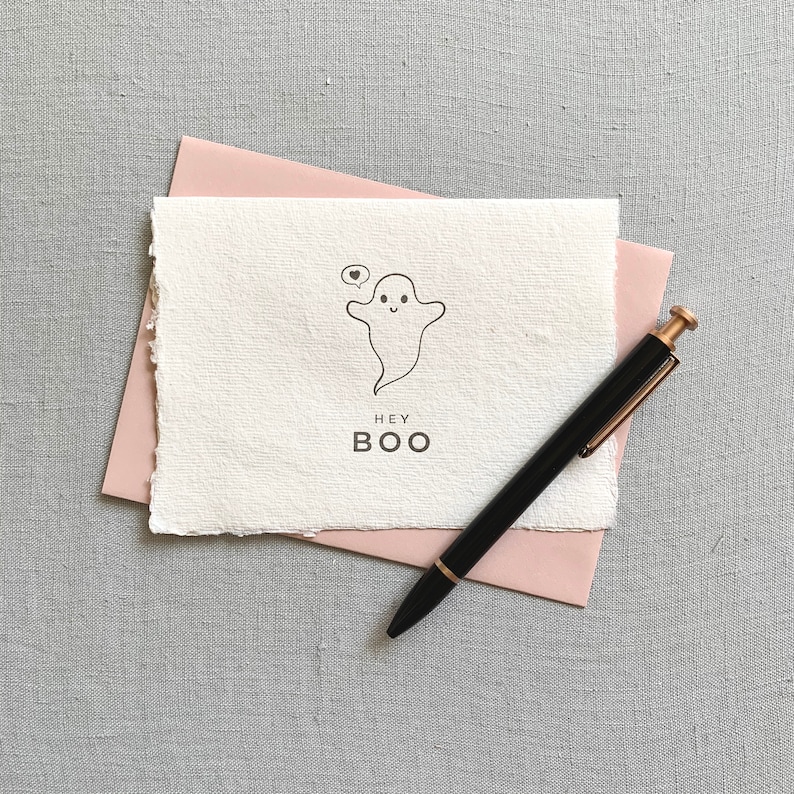 May include: A white card with a simple line drawing of a ghost with a heart in a speech bubble. The text "HEY BOO" is printed below the ghost.