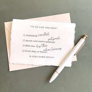 May include: A handwritten to-do list for 2020 on a piece of paper with a white pen. The list includes: Coachella cancelled, Sarah and Jeff's wedding postponed, Hair Cut diy this, online learning, First Day of School. The list ends with the question: IS 2020 OVER YET?!