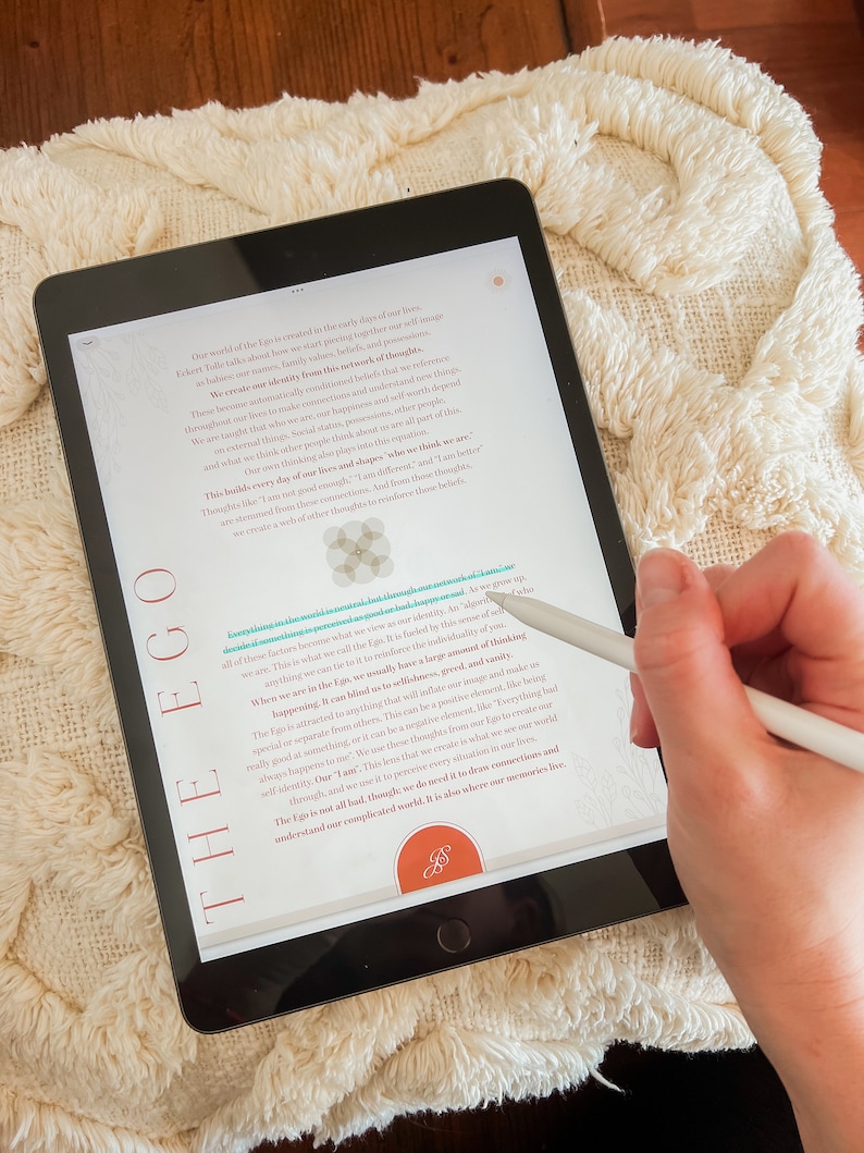 May include: A close-up of a tablet screen displaying text about the ego. The text is in a white font on a black background. The text is about the ego and how it can blind us to our true selves. The text is from the book "A New Earth" by Eckhart Tolle.
