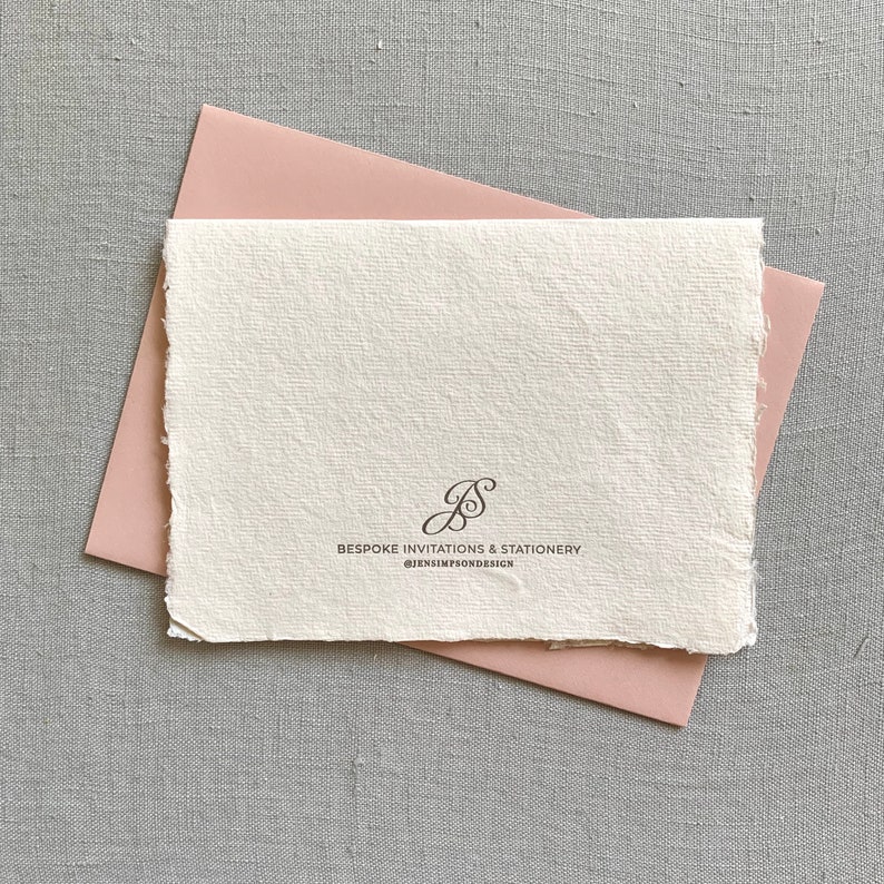 May include: A white card with a pink envelope. The card has a handwritten monogram "JS" and the text "BESPOKE INVITATIONS & STATIONERY @JENSIMPSONDESIGN".