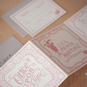 May include: A folded card with a pink and white design. The front of the card features a pink castle with the text "Once Upon a Time..." in a pink script font. The back of the card features the text "Mr. Prince and the Beautiful Princess" in a pink script font.