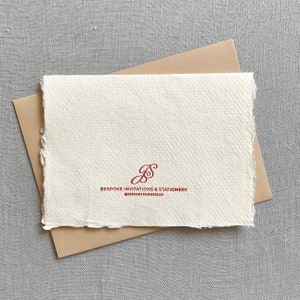 May include: A white card with a brown envelope. The card has a red cursive logo that says "Bespoke Invitations & Stationery" and "@jensinfson.design".