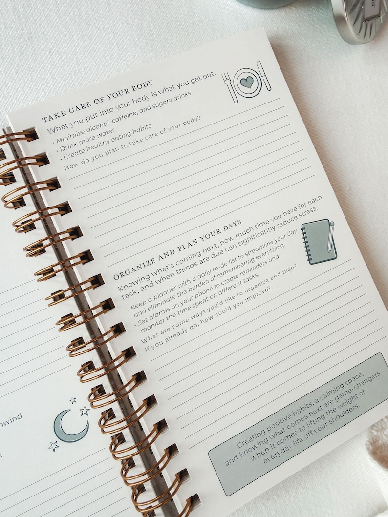 Pu&ograve; includere: Una pagina di agenda con rilegatura a spirale che presenta le sezioni TAKE CARE OF YOUR BODY e ORGANIZE AND PLAN YOUR DAYS. La pagina include aree di scrittura a righe, icone di un piatto con un cuore, un taccuino con una matita e una luna.