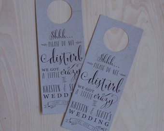 May include: Two brown paper door hangers with a hole at the top for hanging on a door knob. The text on the hangers reads "Shhh... Please do not disturb. We got a little crazy. Kristin & Scott's Wedding."