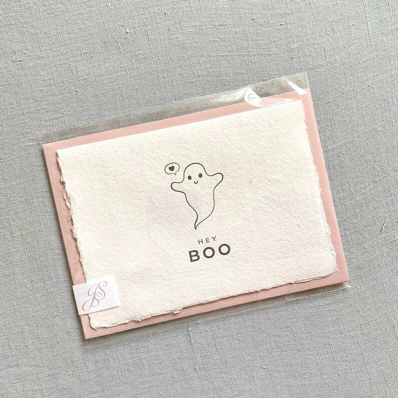 May include: A pink and white card with a cute ghost illustration and the text "Hey Boo".