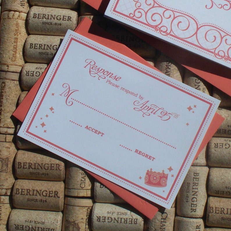 May include: A white RSVP card with pink and red accents. The card has a dotted border and a crown graphic. The text on the card reads "Response Please respond by April 25th".