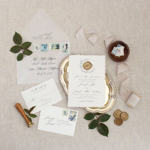 May include: A wedding invitation suite with a white background and calligraphy text. The invitation features a wax seal with a floral design. The RSVP card and envelope are also included in the image.