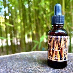 May include: A brown glass bottle with a dropper top and a label that reads "Shatavari Root" and "Renewed Rhythms". The bottle is sitting on a wooden surface with a blurred background of green bamboo.