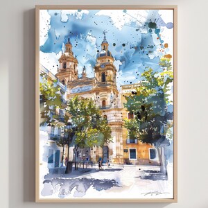 May include: Watercolour painting of a cathedral with twin bell towers, set against a blue sky with paint splatters. The artwork features a detailed depiction of the building's architecture, surrounded by trees and buildings, framed in a light wood frame.