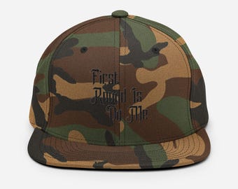 May include: A camouflage-patterned baseball cap with black embroidered text that reads "First Round Is On Me".