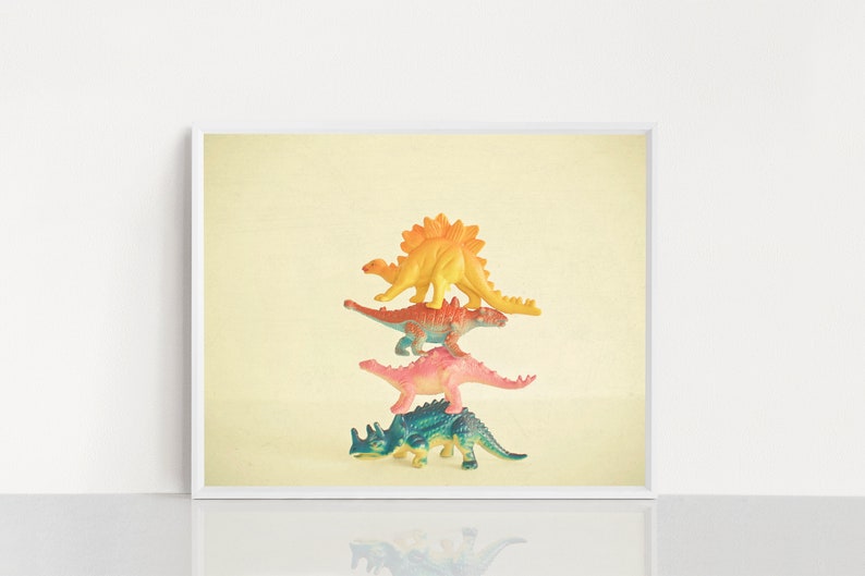 May include: A stack of four colorful plastic dinosaur toys. The dinosaurs are arranged from largest to smallest, with the yellow dinosaur on top and the green dinosaur on the bottom.