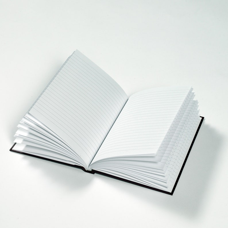 May include: A black lined notebook with a black cover is open and lying flat on a white surface.