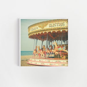 May include: A vintage carousel with colourful horses and a sign that reads "Steam & Electric" on a beach.