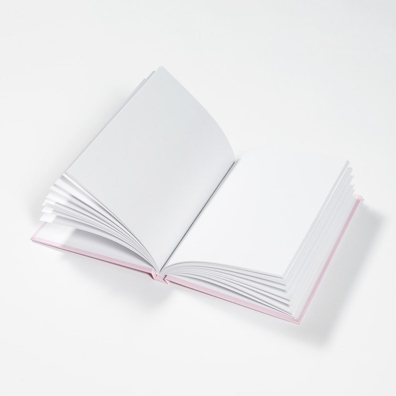 May include: A blank, white book with a pink cover is open to a new page. The book is lying flat on a white surface.