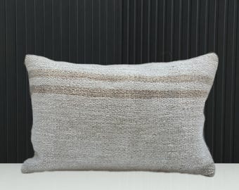 May include: A rectangular throw pillow featuring a textured, light gray woven fabric. The pillow is accented by two horizontal, parallel stripes in a muted tan or beige tone that run across the upper portion of the cushion's front surface.