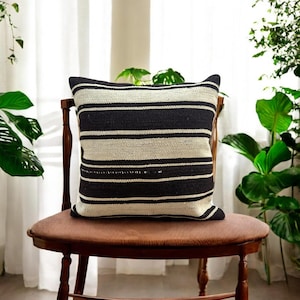 May include: Black and white striped throw pillow with a woven texture. The pillow is sitting on a brown wooden chair.
