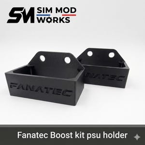 May include: Two black Fanatec Boost kit PSU holders. Each holder has a rectangular box shape with the word "FANATEC" embossed on the front. The holders have two holes at the top and the text "SIM MOD WORKS" is at the top.
