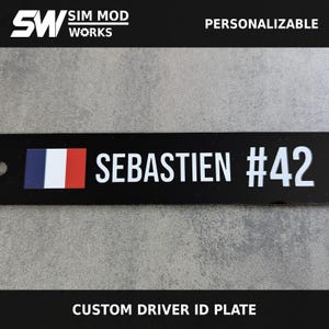 May include: A black rectangular driver ID plate featuring the text SIM MOD WORKS, PERSONALIZABLE, and CUSTOM DRIVER ID PLATE. The plate displays a French flag icon, the name SEBASTIEN, and the number #42 in white sans-serif font on a black background.