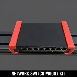 Könnte beinhalten: Ein schwarzer Netzwerk-Switch mit roten Halterungen. Das Gerät hat mehrere Anschlüsse und ist auf einer schwarzen Schiene montiert. Der Text "NETWORK SWITCH MOUNT KIT" wird unten im Bild angezeigt.