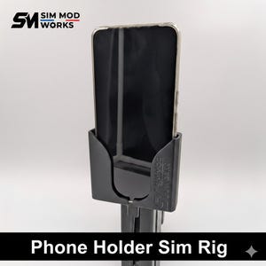 Op de afbeelding: Zwarte telefoonhouder sim rig met een telefoon op zijn plaats. De houder heeft de tekst "SIM MOD WORKS" en "Phone Holder Sim Rig" in het wit. De telefoon zit in een doorzichtige hoes.