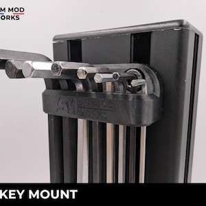 May include: Black hex key mount with a set of silver hex keys. The mount has the text "SIM MOD WORKS" and "HEX KEY MOUNT" in white. The hex keys are in various sizes and are made of metal.