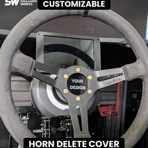 Puede incluir: Un volante de carreras negro con un aro de aspecto de ante y una cubierta central de claxon con el texto YOUR DESIGN. La placa central de metal tiene pernos dorados y el texto DRIFT SHOP. El texto superior dice SIM MOD WORKS CUSTOMIZABLE.