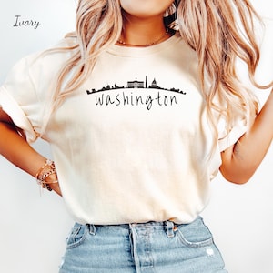 May include: A white t-shirt with a black graphic of the Washington D.C. skyline and the word "washington" written in cursive.