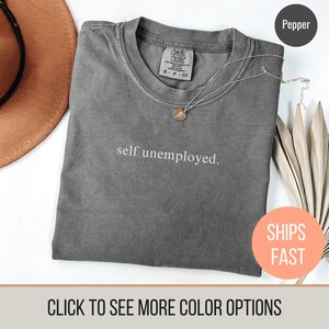 May include: A gray t-shirt with the text "self unemployed." printed in white. The shirt is made of a soft, comfortable fabric and has a relaxed fit.