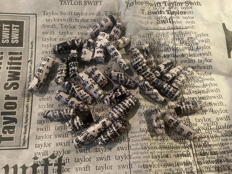 K&ouml;nnte beinhalten: Eine Sammlung kleiner, wei&szlig;er Papierrollen mit schwarzem Text darauf. Die Rollen sind aufgerollt und haben eine leicht strukturierte Oberfl&auml;che. Der Text auf den Rollen ist haupts&auml;chlich der Name "Taylor Swift", der viele Male wiederholt wird.